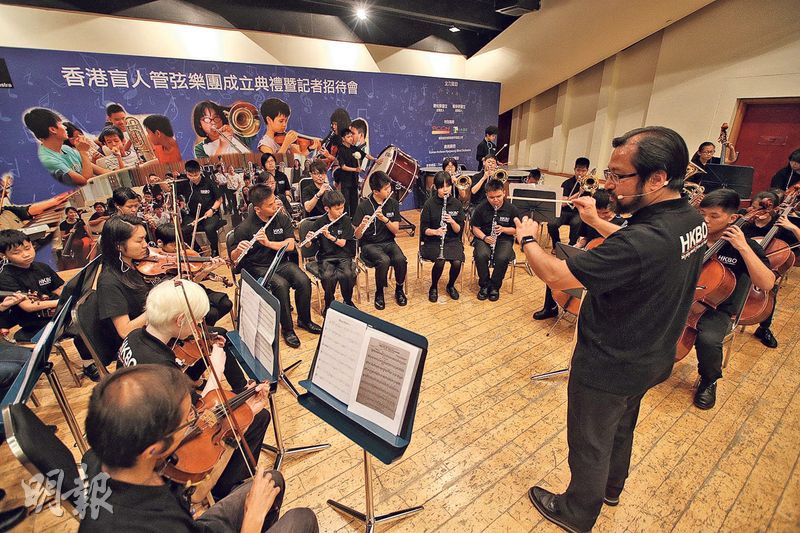 香港盲人管弦樂團音樂總監杜永政（前右一）在成立典禮上用耳機指揮視障樂團。31名團員與6名樂團導師共同演奏柴可夫斯基《花之圓舞曲》。（曾憲宗攝）